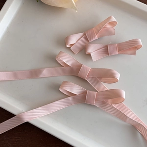 Détail de quatre barrettes à nœuds en ruban rose pastel sur un plateau blanc