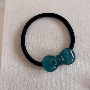Close-up of a dark green resin bow hair tie with a black high-elastic band on canvas