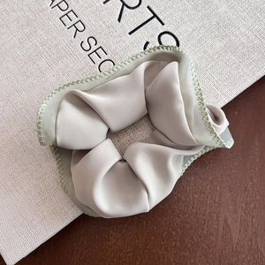 Detailed view of beige satin scrunchie with green zigzag stitching on white background