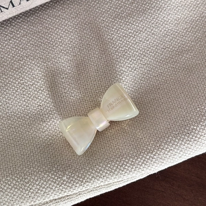 Macro detail of pearlescent white bow hair clip with France Handmade engraved text