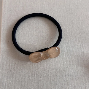 Detail of amber resin bow tie charm on a high-elastic black hair tie for daily wear