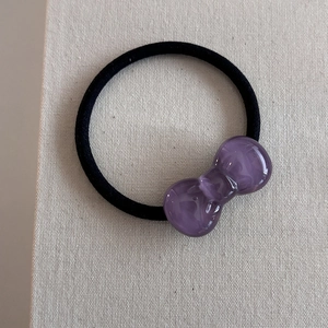 Detail shot of a small purple resin bow hair tie with a black elastic band on fabric