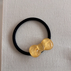 Close-up of yellow resin bow detail on a black elastic hair tie with a textured fabric background
