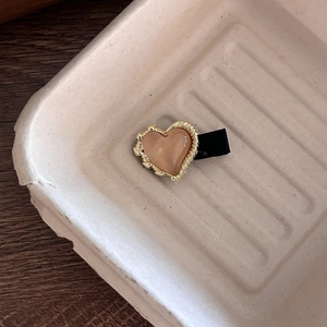 Detailansicht einer herzförmigen Haarklammer mit goldenem Kordelrand und glatter Harzeinlage