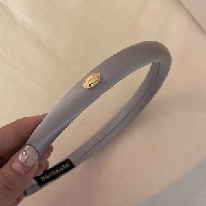 Detail of light purple headband with golden metal tag and handmade logo embroidery