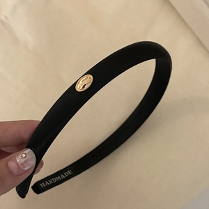 Close-up of black satin headband with gold metal badge and handmade woven label