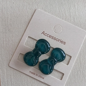 Close-up of small dark teal resin bow hair clips on a light beige display card