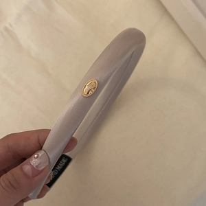 Detailed close-up of light gray satin headband with a golden logo and handmade label