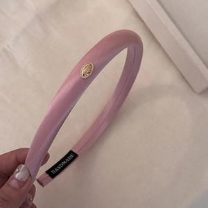 Detail of pink satin padded headband featuring a gold emblem and handmade woven label