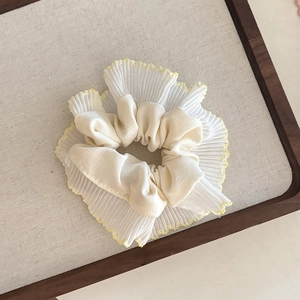 Detail of cream organza scrunchie with yellow wavy edge stitching on wooden tray