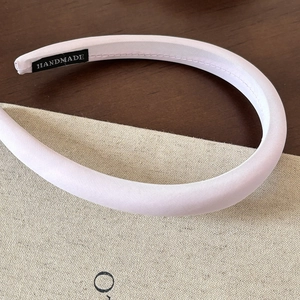 Close-up of handmade pink satin headband showing fine fabric texture and woven brand label