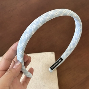 Detail of light blue plaid headband showing the handmade label on wood background