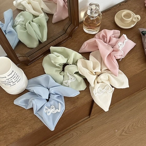 Set of four pastel bow scrunchies with white lace embroidery on a wooden surface