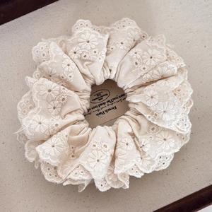 Macro view of high-quality floral embroidery and lace texture on a beige scrunchie