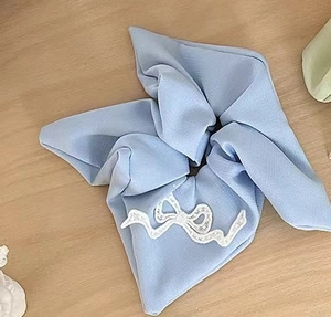 Detail shot of a light blue chiffon scrunchie with white lace bow on a wooden surface