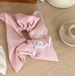 Close-up of pink fabric scrunchie with white lace edges on light wood tabletop background