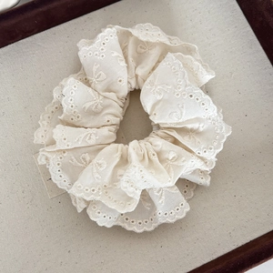 Detailed macro view of cream-colored cotton lace scrunchie with floral embroidery and bow