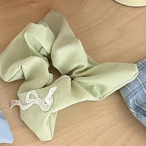 Detail of light green chiffon scrunchie with white lace bow on a light wooden background