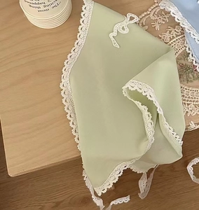 Détail d'un foulard vert clair avec bordure en dentelle blanche et broderie nœud