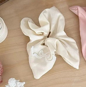 Detail of a beige bow hair scrunchie with delicate lace embroidery and fabric folds
