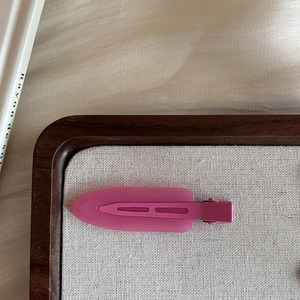 Matte pink duckbill hair clip for women on a beige linen surface in warm home setting
