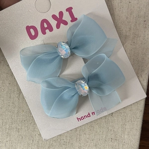 Detailed macro view of two blue chiffon bow hair clips with rhinestones on a display card