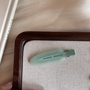 Minimalist matte mint green duckbill hair clip on a wooden display tray for women