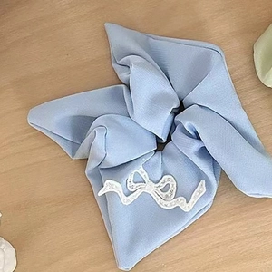Elegant light blue scrunchie with a white lace bow detail on a minimal wooden background