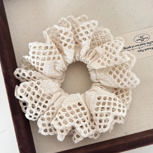Detail of multi-layered cream lace scrunchie with intricate hollow embroidery on a wooden tray