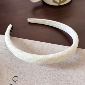 Detailed view of handmade cream plaid fabric headband with a woven label on a wooden desk
