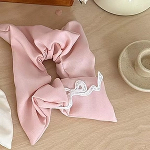 Pink bow hair scrunchie with lace edges and fabric texture on a wooden desk