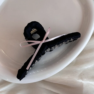 Large black fabric hair claw clip with a delicate pink ribbon bow in a ceramic tray