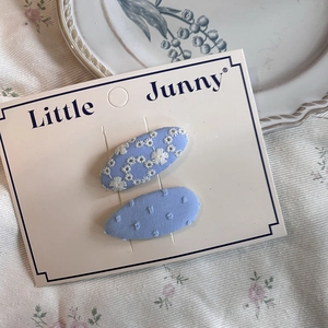 Close-up of blue embroidered hair clips with white daisies and polka dots on card