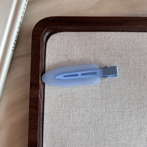 Close-up of matte blue-grey seamless hair clip on a minimalist wooden tray display