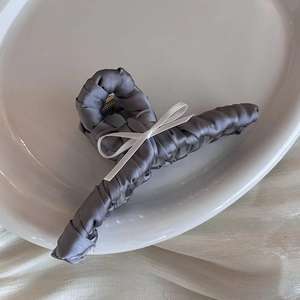 Close-up of grey satin hair claw clip with a white bow detail on a white ceramic dish