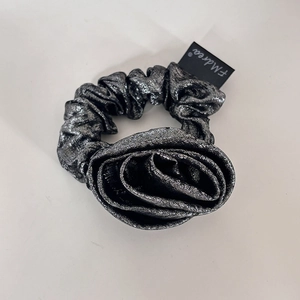 Detailed macro view of dark grey metallic fabric flower scrunchie with brand logo tag
