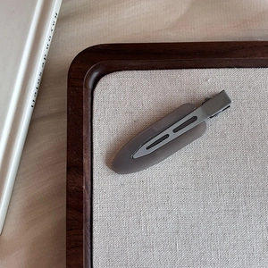 Close-up of a matte pastel pink duckbill hair clip on a white linen texture board