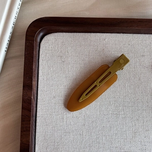 Detail of amber resin oval hair clip with mustard green metal duckbill clip design