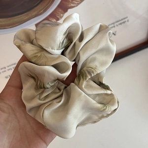 Large silk scrunchie with green plant leaf prints shown held in hand for hair styling