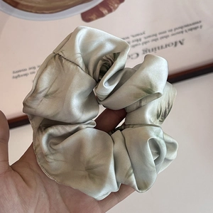 Detail of a large silk scrunchie with pink and green ink-wash patterns in hand