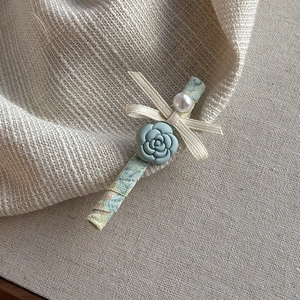 Detail of floral fabric hair clip with a blue rose, white pearl, and ribbon bow