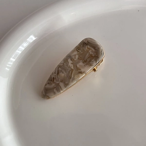 Detailed view of handmade acetate marble hair clip with gold metal base and engraving