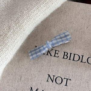 Detail of blue plaid hair clip with shimmer finish on cream canvas and knit fabric