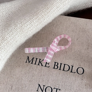 Detailed macro view of a pink striped bow hair clip with pearlescent finish on linen