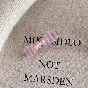 Close-up of pink and white checkered bow hair clip on beige linen texture background