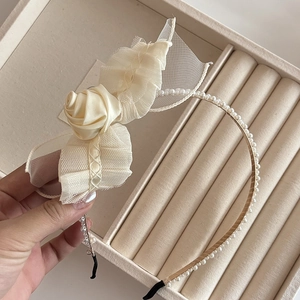 Detail of elegant cream headband with white pearls, satin rose and mesh bow on display