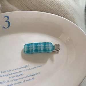 Blue and white checkerboard acetate hair clip on a white ceramic tray with soft lighting