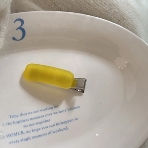 Detail of yellow matte rectangular hair clip on white porcelain plate with metal clip