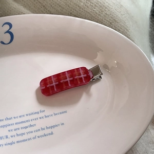 Macro view of red checkered acetate hair clip on a white ceramic plate with metal back