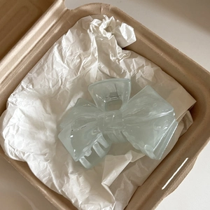 Detail view of a cream blue translucent bow-shaped hair claw clip in a gift box